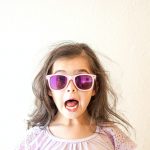 girl in white and purple floral crew neck shirt wearing blue framed sunglasses